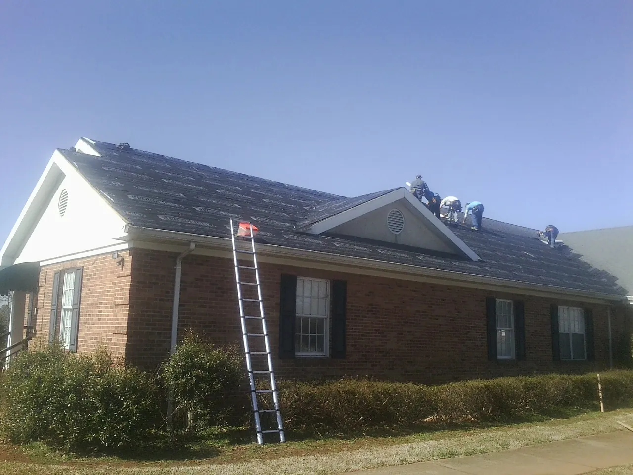 Crew tearing shingles off a brick ranch roof with a ladder set — Emergency Roof Repair work by our crew in Bradfordwoods