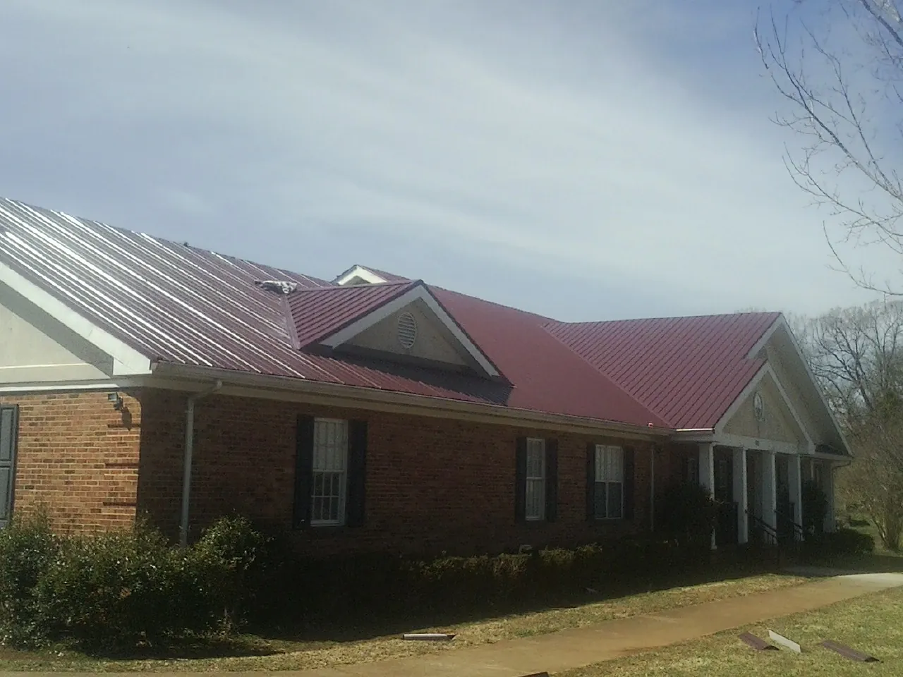 Red metal roof with gabled entries on a long brick building, from a Hail Damage Roof Repair job in Bradfordwoods