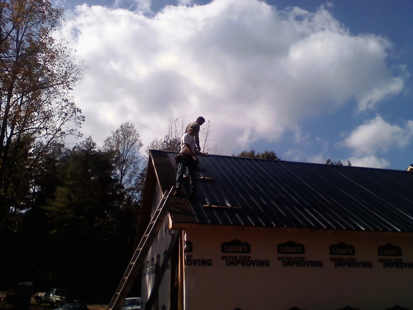 Roofer fastening dark metal panels high against a cloudy sky, from a Roof Inspection job in Bradfordwoods