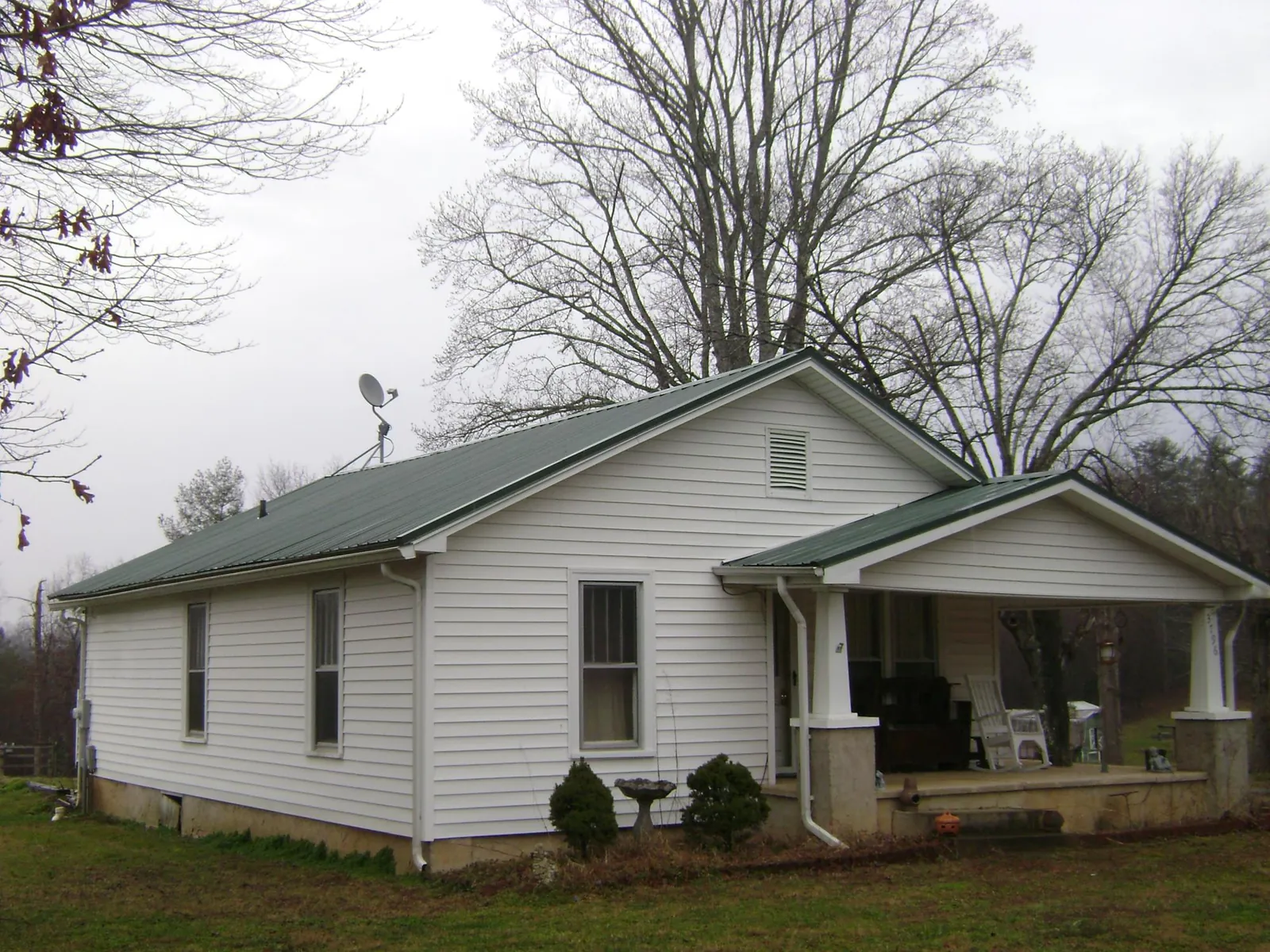 Green metal roof on a white bungalow with a side porch in Bradfordwoods