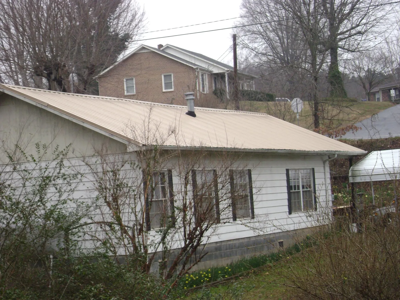 Tan metal roof on a white sided house set into a hillside — Commercial Roofing by Roofing Brothers in Bradfordwoods